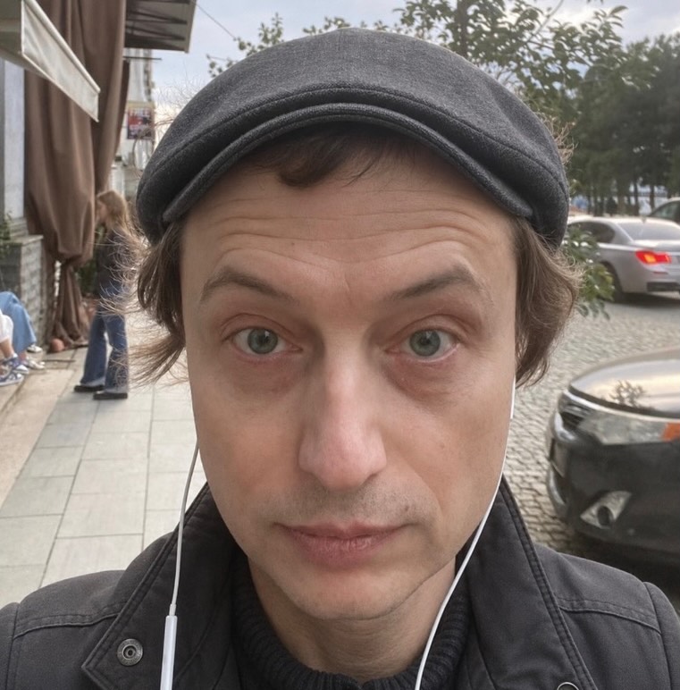 Denis Ostapenko ao ar livre, de boina cinza e fones de ouvido.